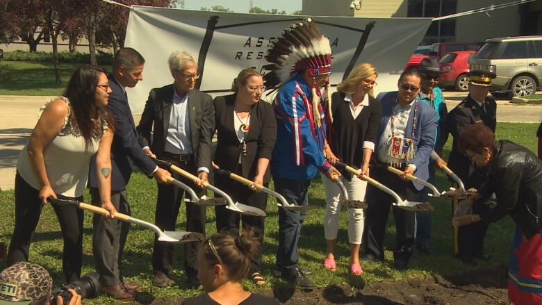 Eight people in a line hold shovels after breaking ground for the memorial.