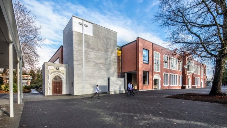 A school with a large cross on the front of the building and a person walking in the foreground.