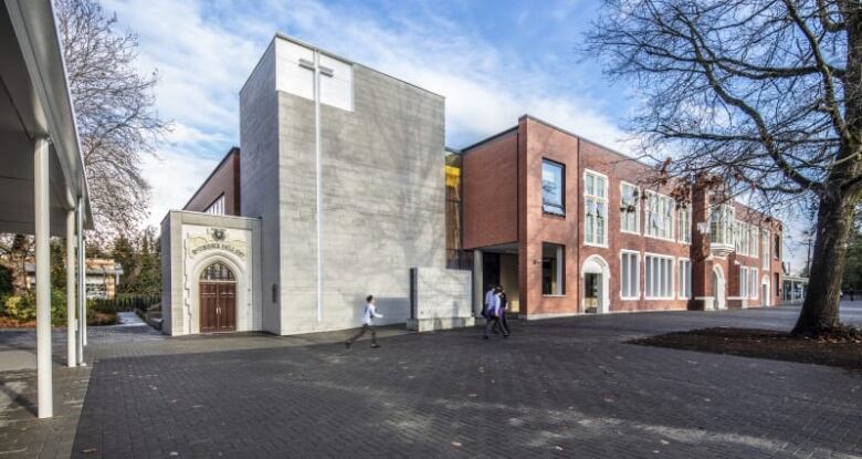 A school with a large cross on the front of the building and a person walking in the foreground.