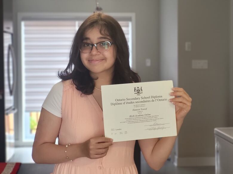 A teenage girl holds her high school diploma.