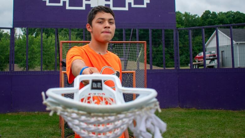 A person standing, pointing a lacrosse stick at the camera. 