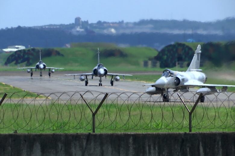 Three fighter jets are seen on the runway of an airbase. 