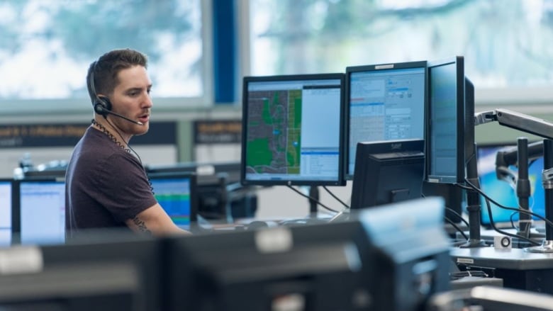 A dispatcher with a headset looks at a number of screens in a dispatch centre.