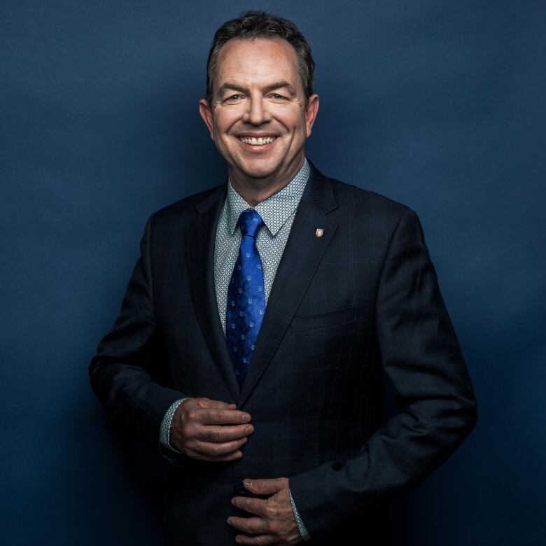 A headshot of Peter Scott. He is smiling and wearing a dark blue suit jacket, a light-coloured patterned shirt, and a vibrant blue tie.