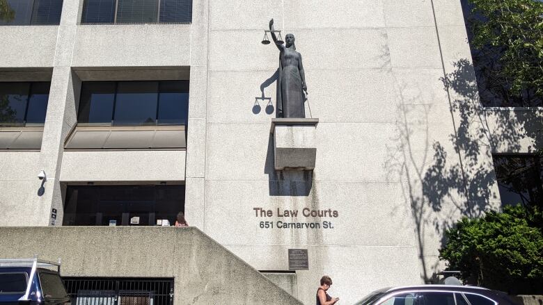 A statue of the Roman god of justice, who is carrying scales and blindfolded, hangs outside a courthouse building.