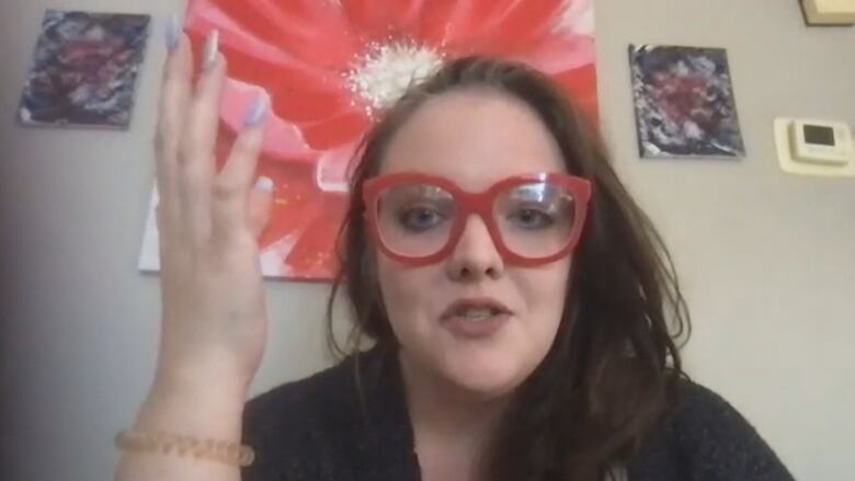 Tech workers Elizabeth Brunet is seen in a screen capture from a Zoom interview. She's wearing thick red glass, gesturing with her right hand and has dark hair.