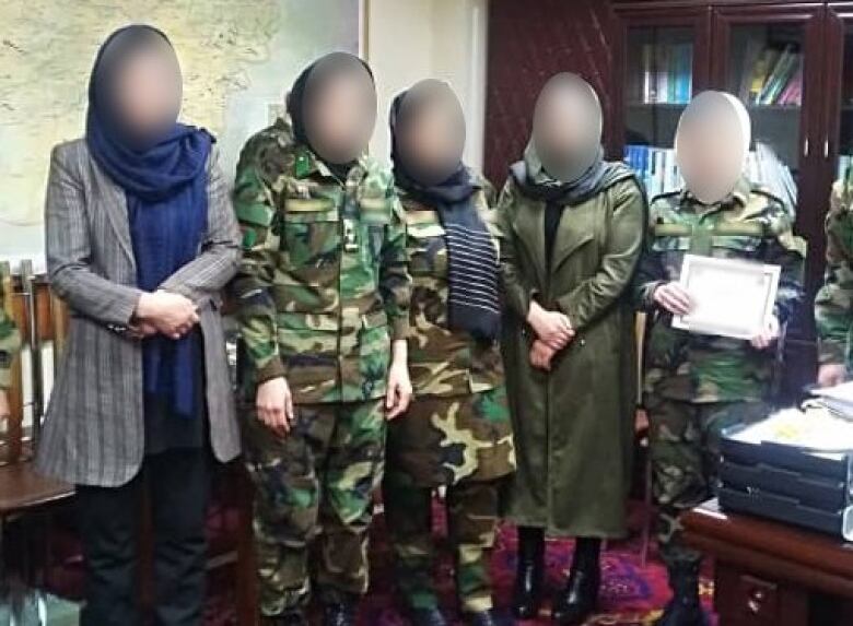 Five women stand side by side with their faces blurred. Some are wearing military uniform.