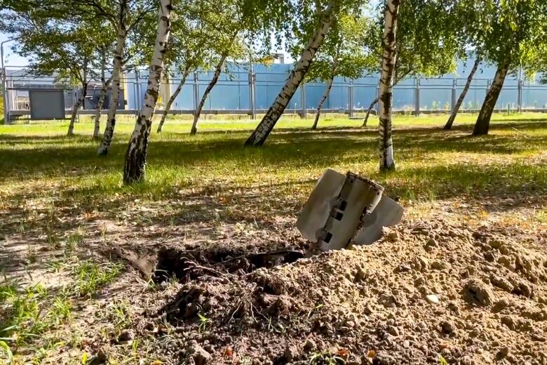 A piece of rocket in the dirt in front of a power station.