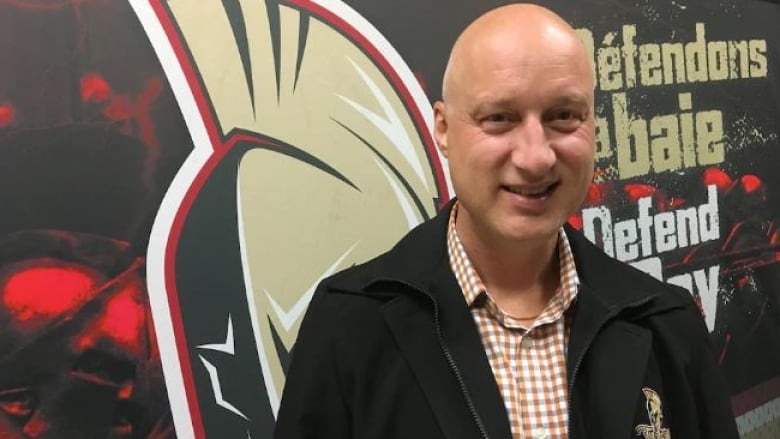 A man stands in front of a Titan logo. 