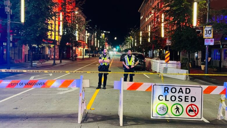 Two police officers wearing safety vests stand behind a sign that says 