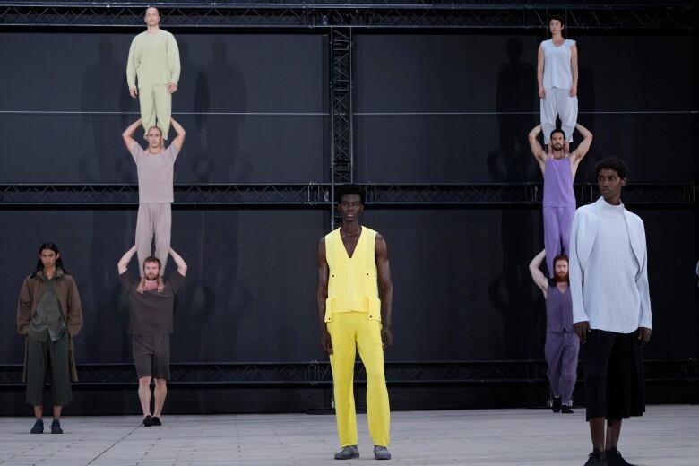 Male models, including some standing on the shoulders of other models, are shown in garments of several colours.