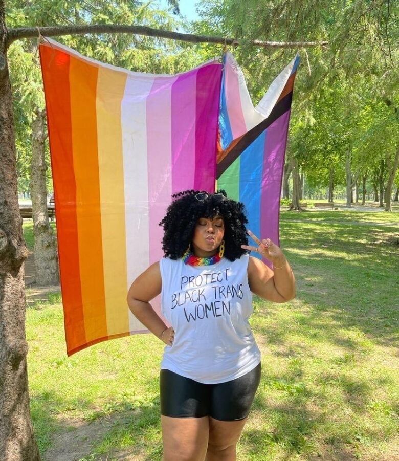 A person holds up the peace sign in front of a rainbow flag.