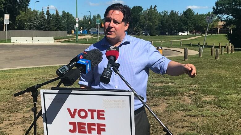 Man speaks at a podium infront of a park