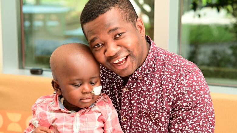 A father holding a toddler. The toddler has a breathing tube attached. 