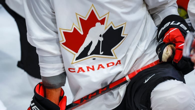 A closeup of a player wearing a Hockey Canada jersey, and wielding a hockey stick. 