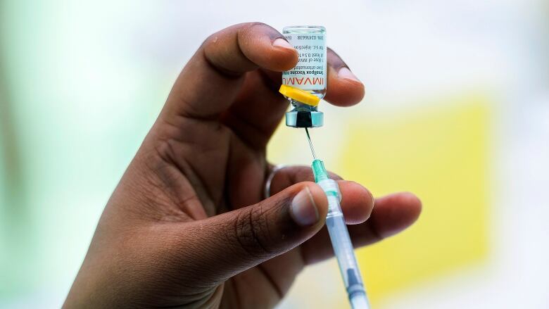 A closeup of a hand holding a syringe, drawing vaccine from a small bottle.