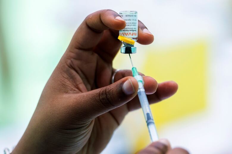 A closeup of a hand holding a syringe, drawing vaccine from a small bottle.