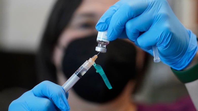 A nurse in a black mask prepares a dose of an mpox vaccine.