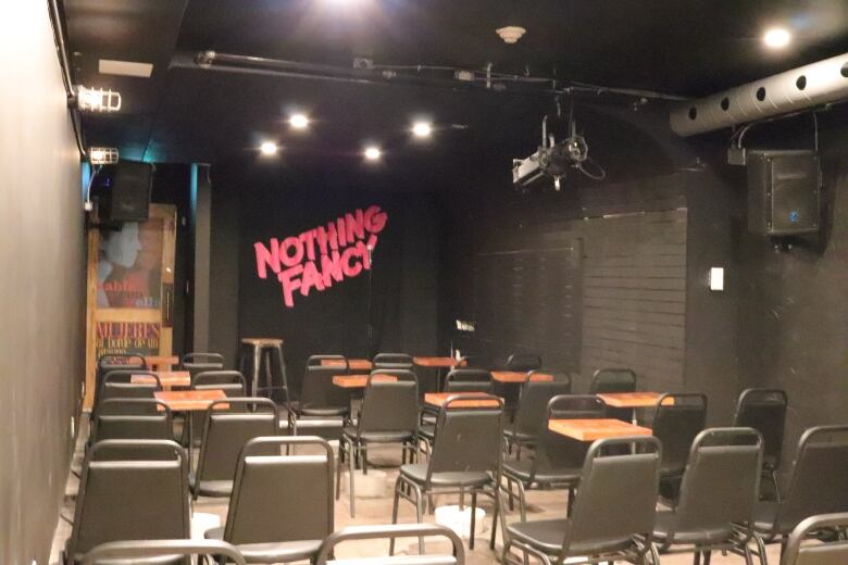 Photo of a small empty room filled with chairs. The walls are painted black. The wall at the front of the room is splashed with a sign that reads in red letters 