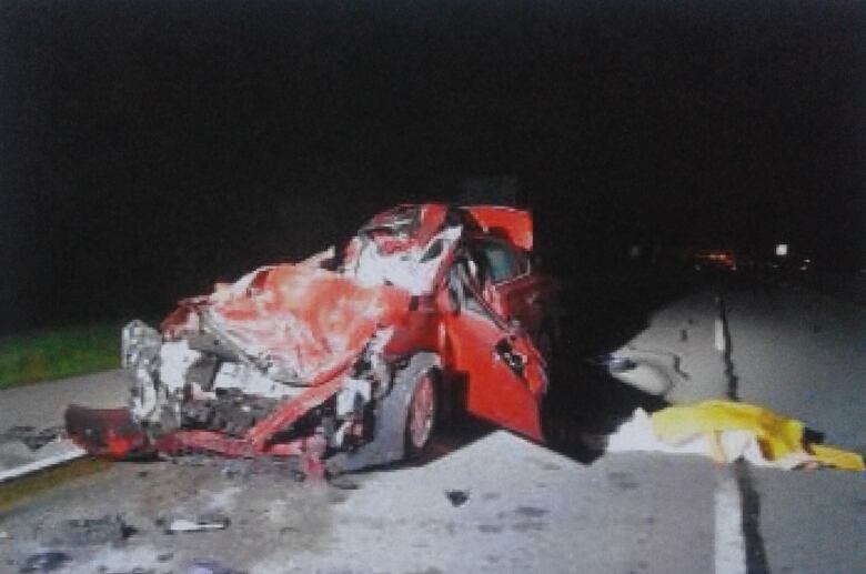 A completely destroyed red car, whose front has been compressed by an impact.