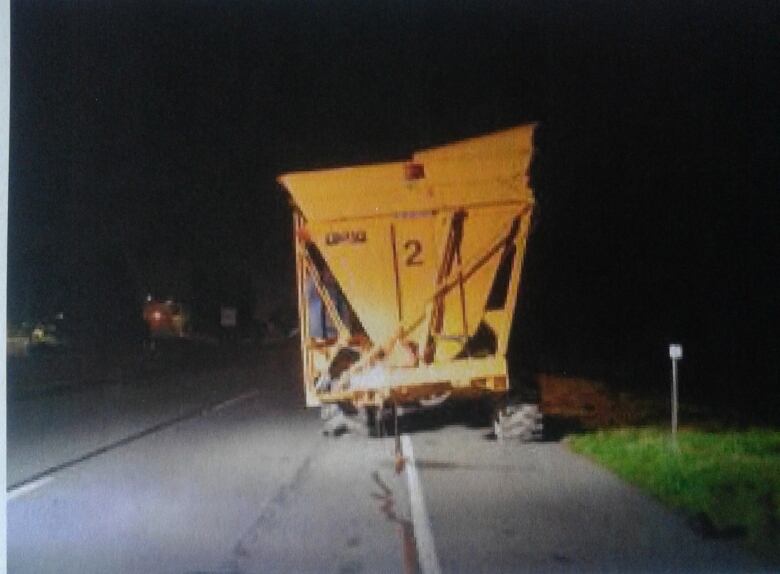 A picture of a yellow utility vehicle from behind, on the side of a rural road.