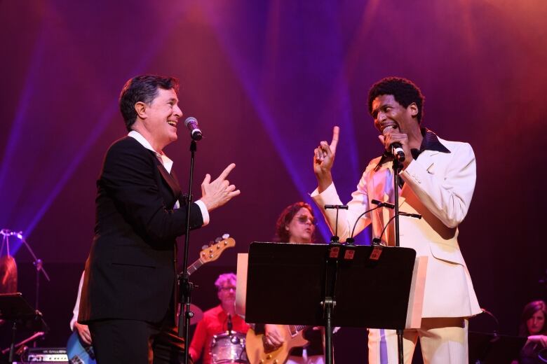 Two men smiling on stage and looking at each other mid-song.