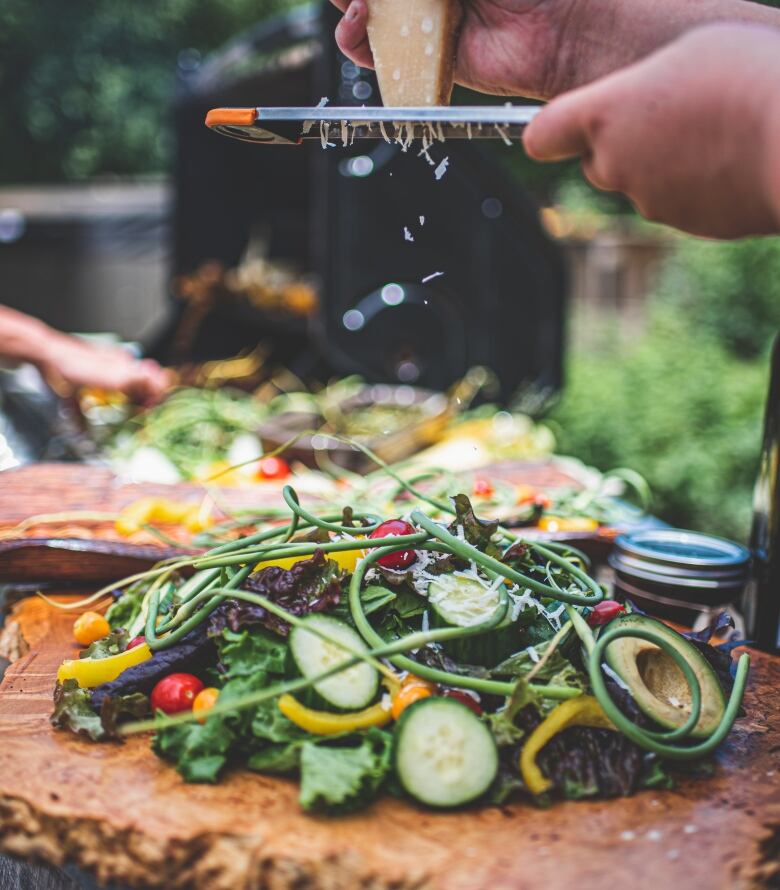 A person grades cheese over a colourful, Mediterranean salad.