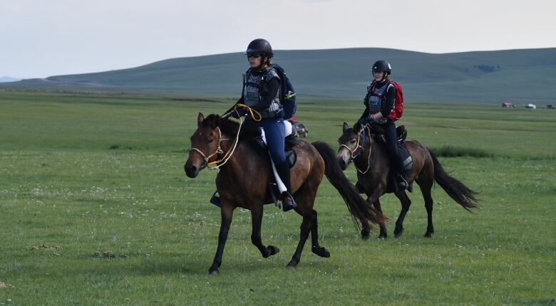 Two women ride horses through the Mongolian countryside.