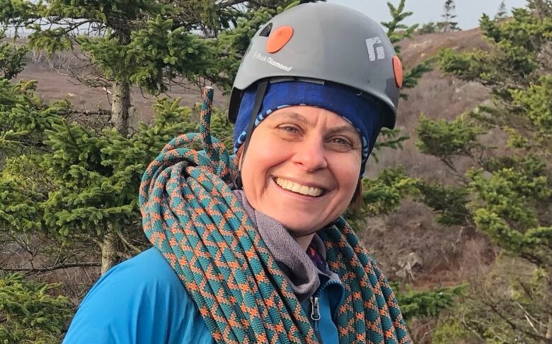 A woman wearing a helmet smiles as she holds onto a climbing rope.