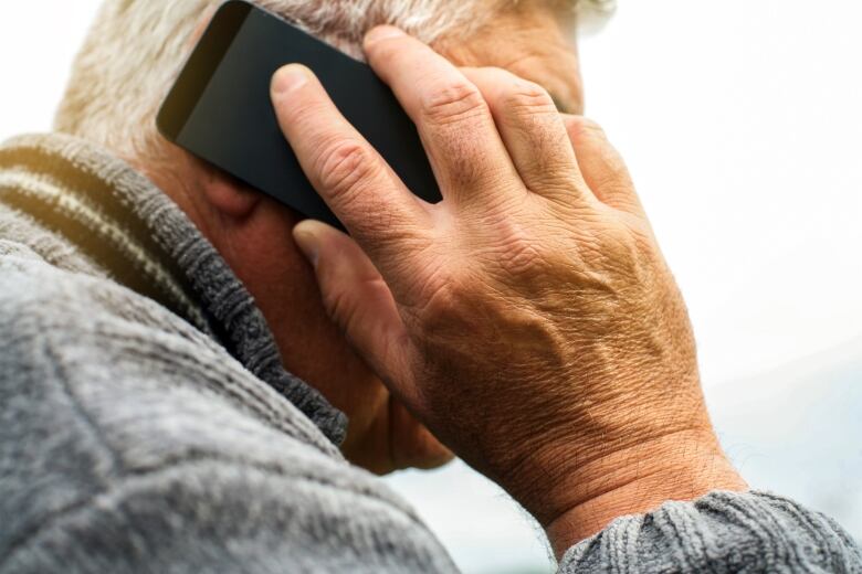 A closeup of a white-haired man in a sweater holding a cellphone up to his ear.