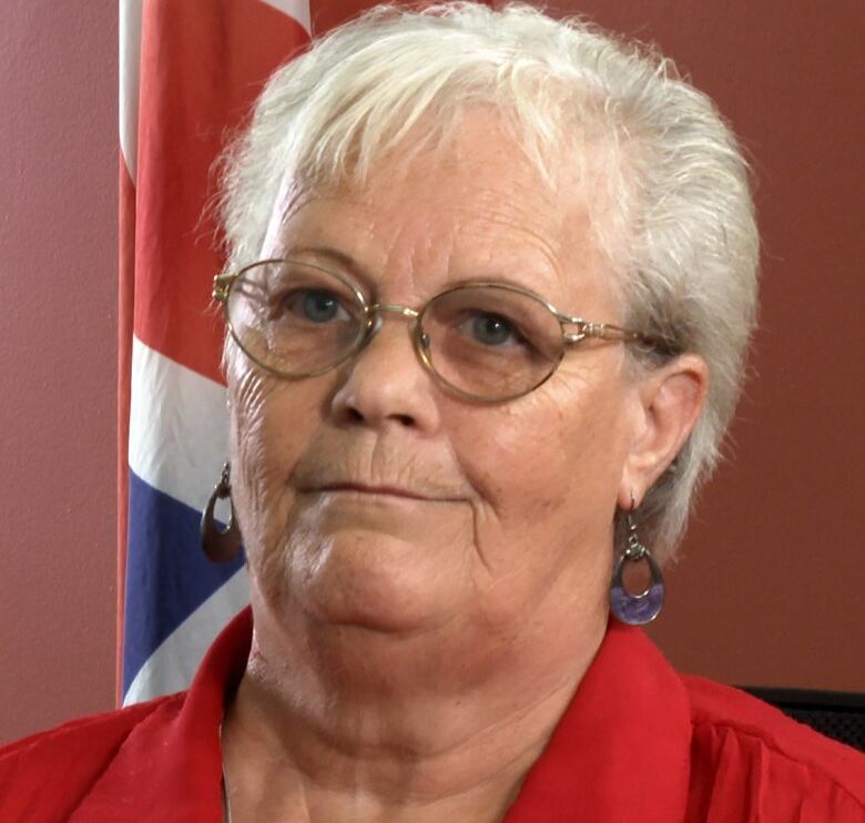 A woman with a red shirt and glasses looks past the camera. 