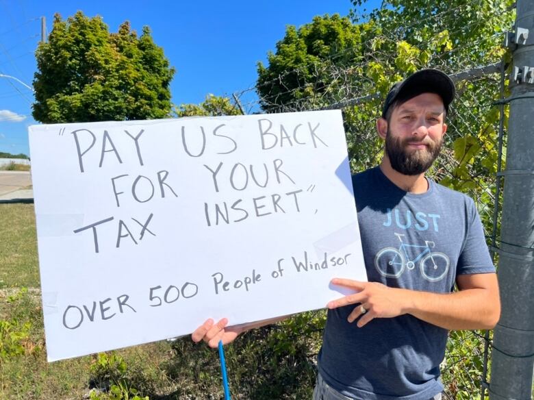 A man in his early thirties holds a sign that says 