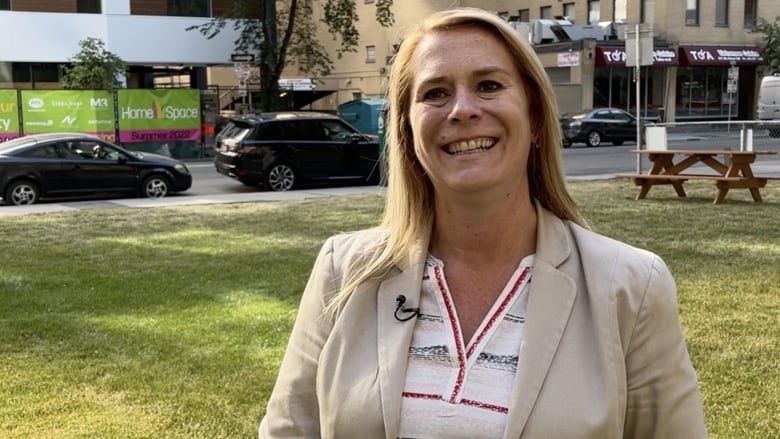 A woman stands in a park, smiling.