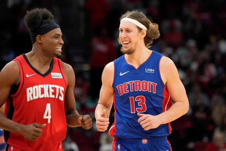 Danuel House and Kelly Olynyk smile in basketball kits. Danuel's is red and has the word 'ROCKETS' on it, Olynyk's is blue and has the word 'DETROIT' on it.