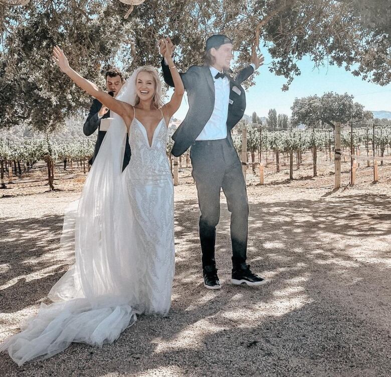 A woman in a wedding dress holds the hand of a man with a backwards hat and sneakers. He is wearing a suit.