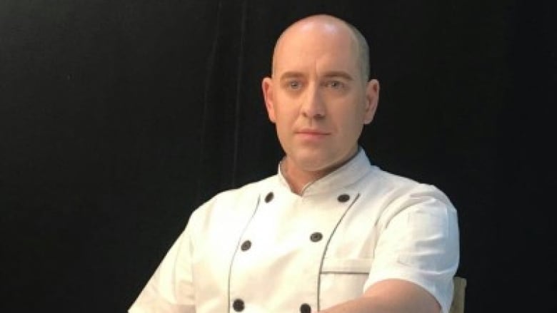 Andrew Eyre sits in a chair. He is a bald white man wearing a chef's uniform.