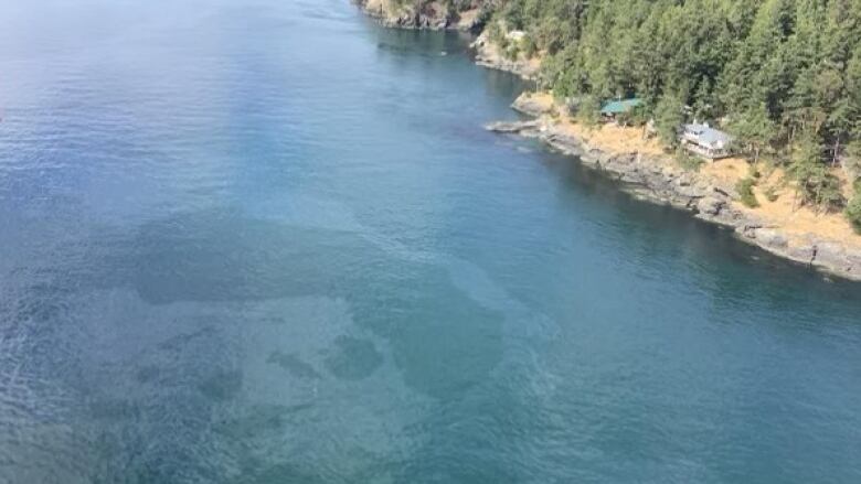 In an aerial image, a clear oil sheen is seen on seawater near a large island.