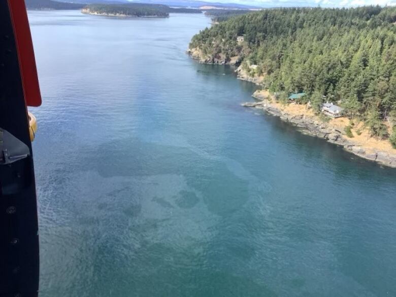 In an aerial image, a clear oil sheen is seen on seawater near a large island.