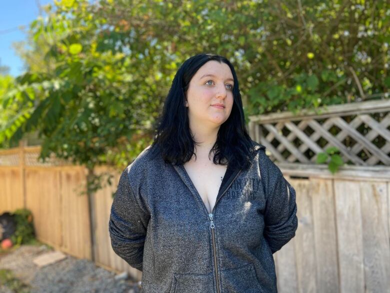 Hailey Gallant, a white woman with black hair, poses in front of a fence.