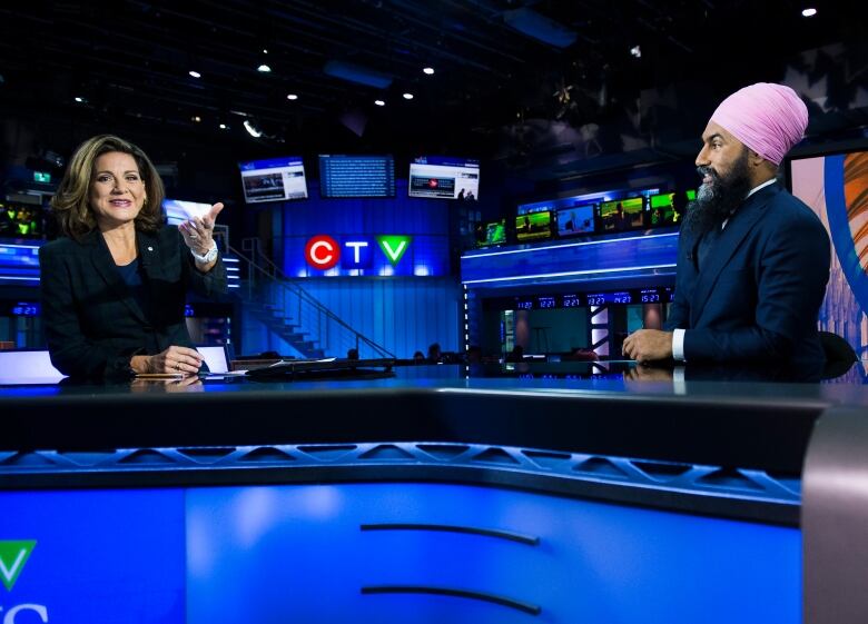 Two smiling people are seated at a news desk, with TV monitors and the CTV logo visible behind them. 