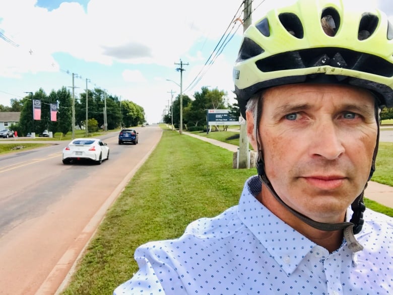 Man in yellow bike helmet with cars going by on street behind him.