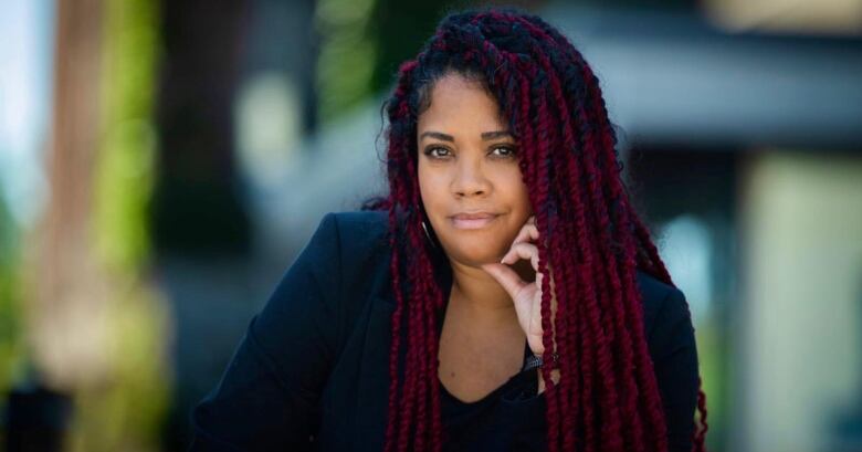 A woman with braids in her hair looks at the camera with her hand on her chin. 