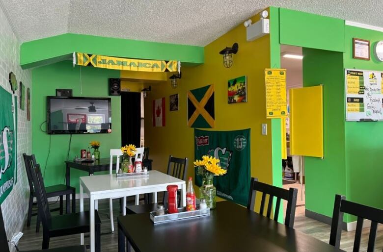 A green- and yellow-painted restaurant dining room is decorated with Saskatchewan Roughriders, Canadian and Jamaican flags, and a banner that says 'Jamaica.'