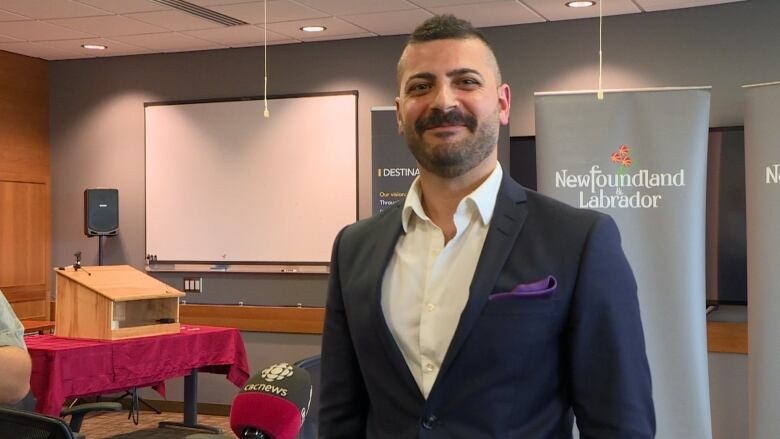 Dr. Sohaib Al-Asaaed standing in a lecture hall at Memorial University with Government of Newfoundland and Labrador signs in the background. 