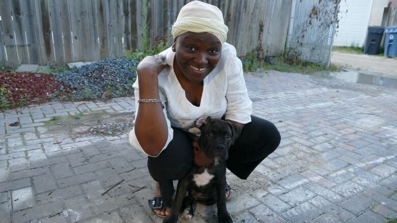 A woman smiles as she crouches down with a puppy.