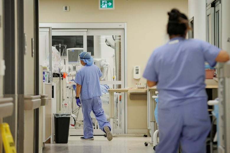 Two nurses stand in a hospital hallway.