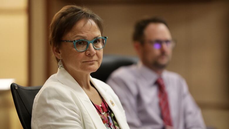 Woman in glasses and white blazer sits at chair in city council