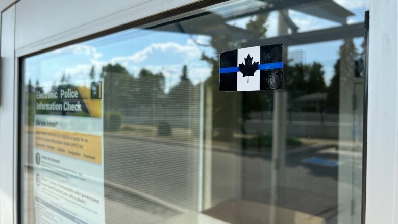 A thin blue line decal, adarkened Canadian flag with a blue line through the middle,  sticks to the glass of a public entry to the District Two office. 