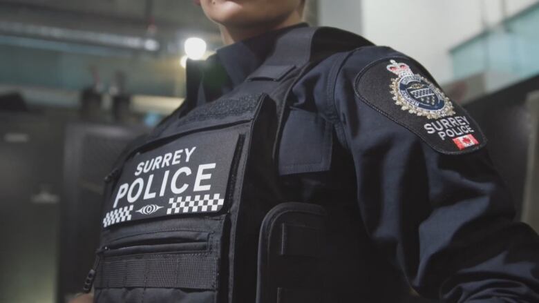 A close up picture of an officer wearing a vest that reads 'SURREY POLICE' on it.