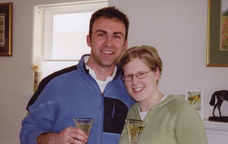 A man and a woman holding fancy drink glasses stand in a kitchen. 